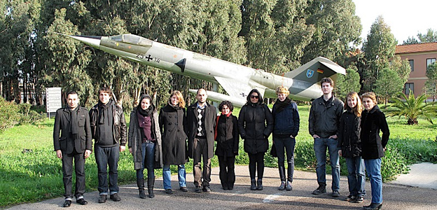 Susanna Schoenberg and the others artists who joined the returnable workshop in Sardinia posing with a warplane in the background